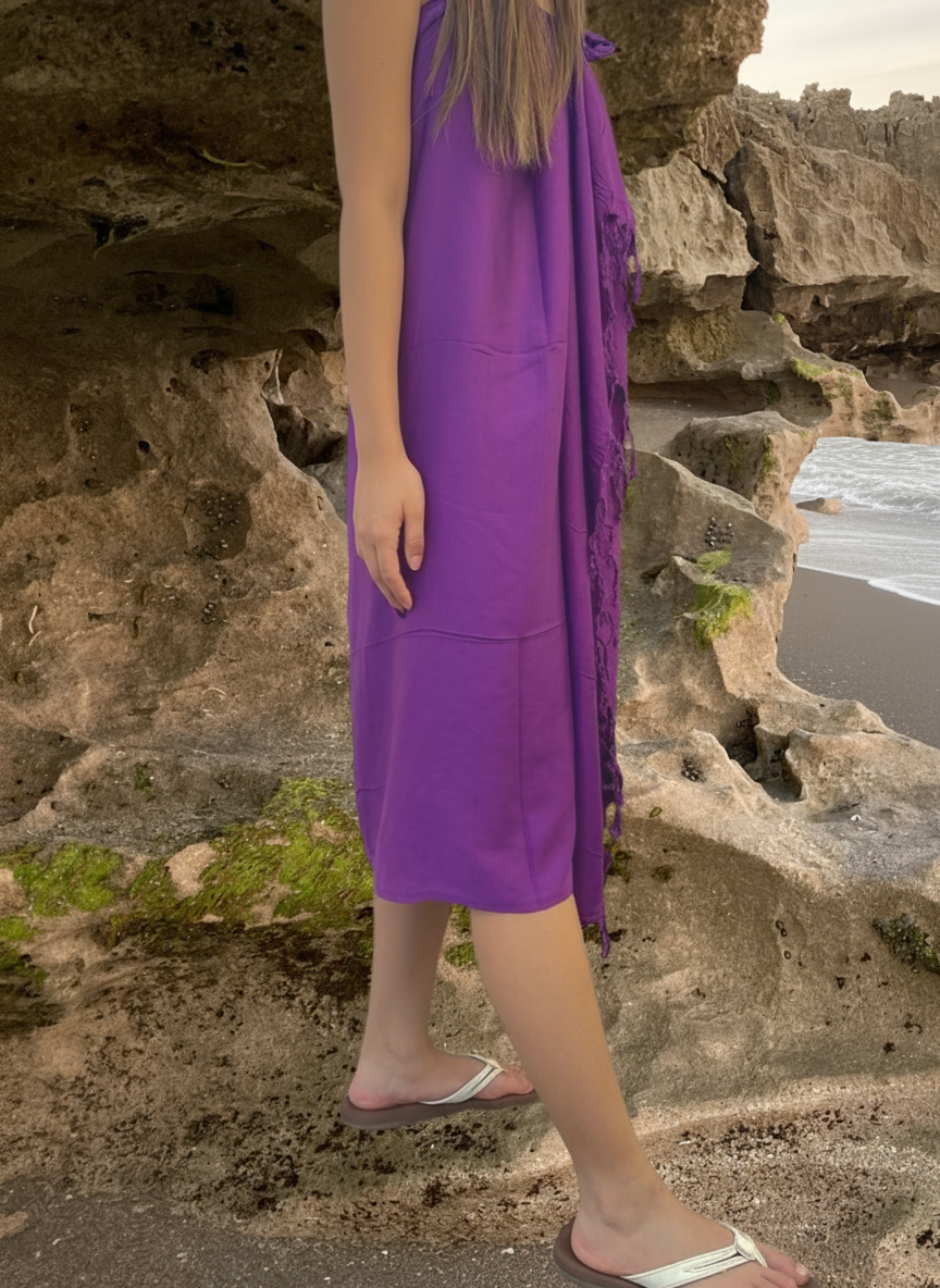 Person wearing a purple dress standing on a rocky beach.