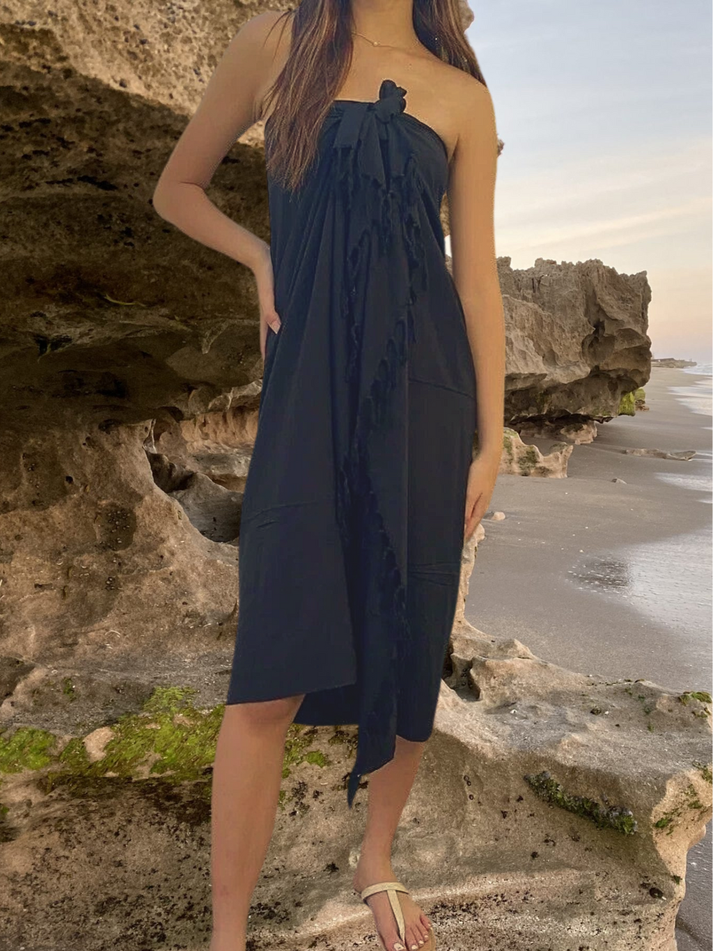 Woman in black pareo sarong dress standing on a rocky beach.